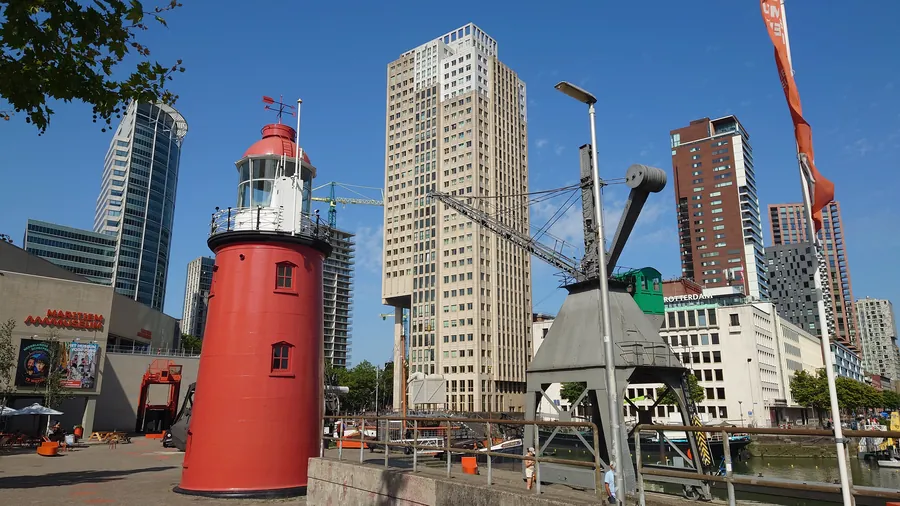 Historic red lighthouse outside the Maritime Museum Rotterdam at Leuvehaven, with the city skyline and a harbour crane behind it