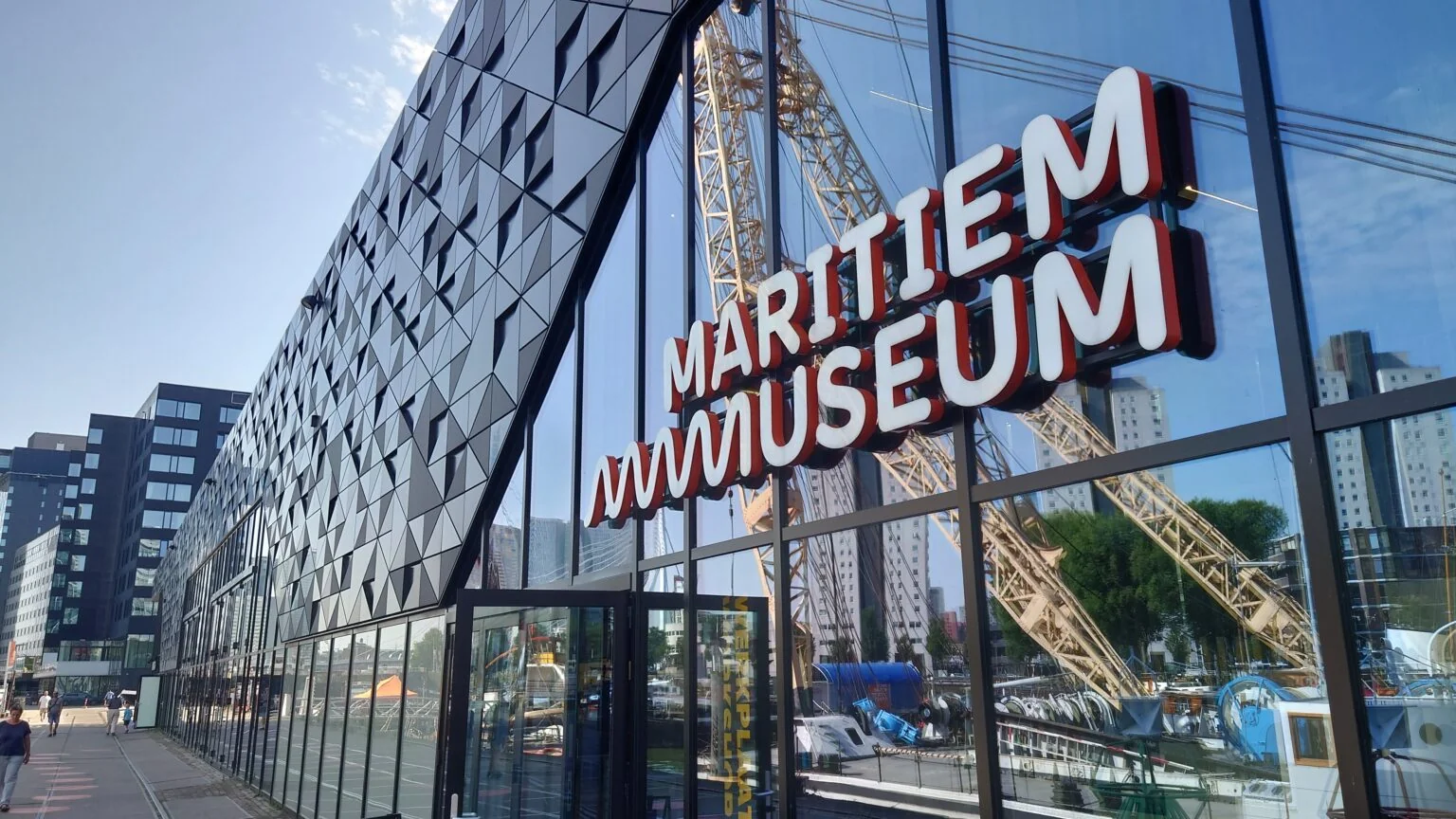 Glass facade of the Maritime Museum Rotterdam (Maritiem Museum) at the historic harbour, with a dockside crane in the background